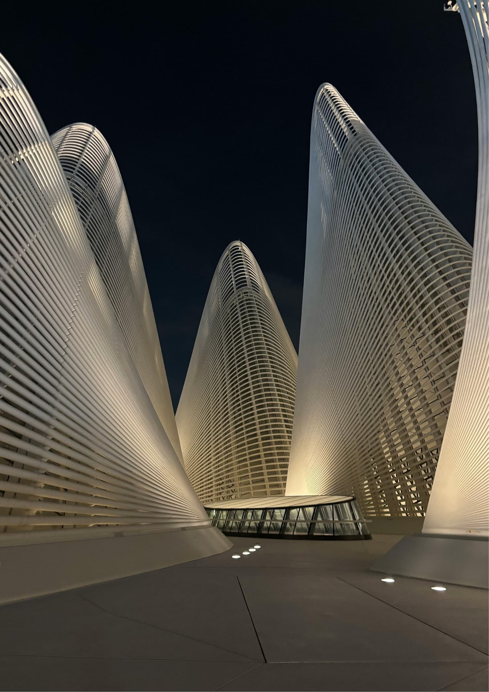 Sweeping curved concrete floor plates on tapered columns around a pale limestone courtyard, one figure walking through